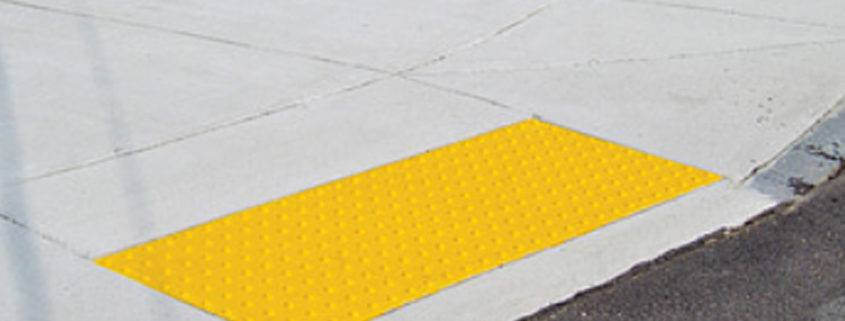 A sidewalk curb ramp which has a yellow detectable surface ramp installed