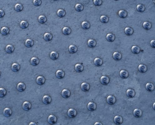 A close-ip of a truncated dome pattern on a silver metallic tactile warning surface