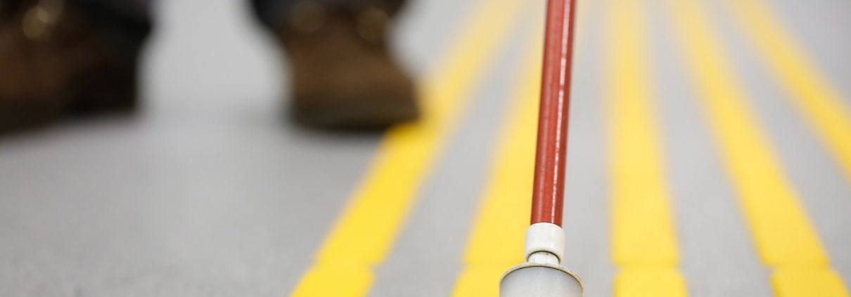 white walking cane positioned between tactile yellow lines
