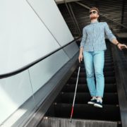 Blind person with long cane on escalator indoors