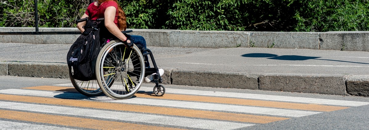 A young woman in a wheelchair in front of a high curb at a pedestrian crossing