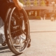 cropped panoramic view of man using wheelchair with bag on street with sunlight