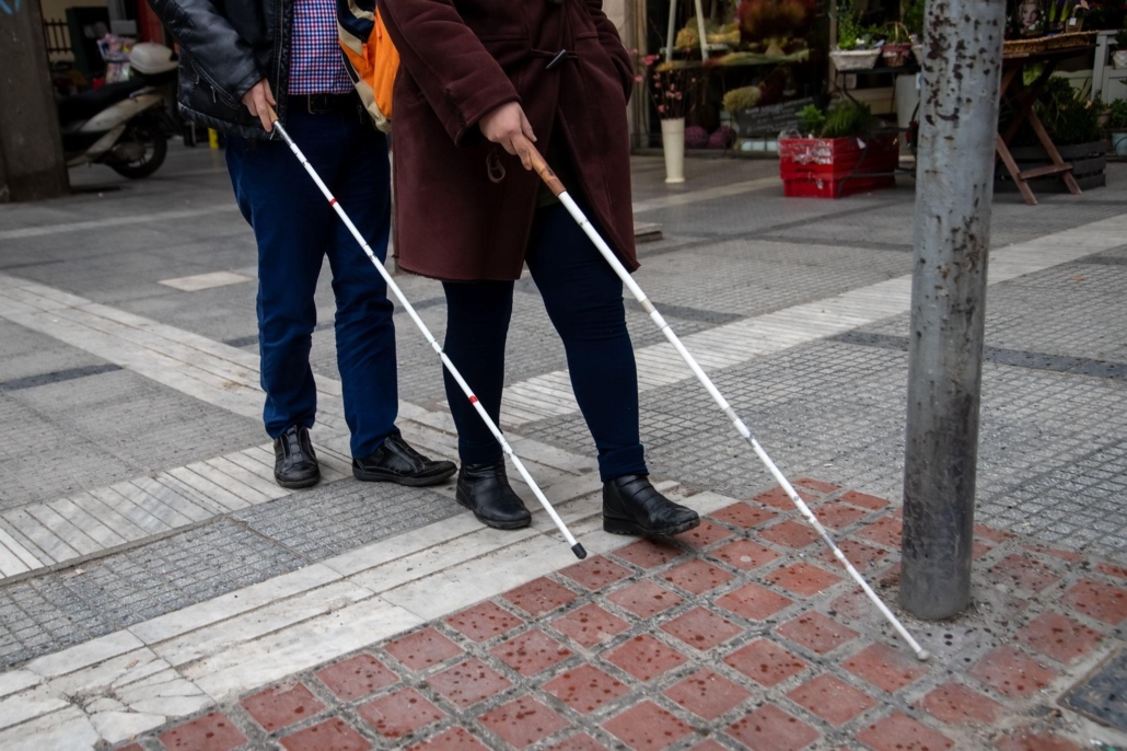 blind man and woman walking on the street using a white walking stick