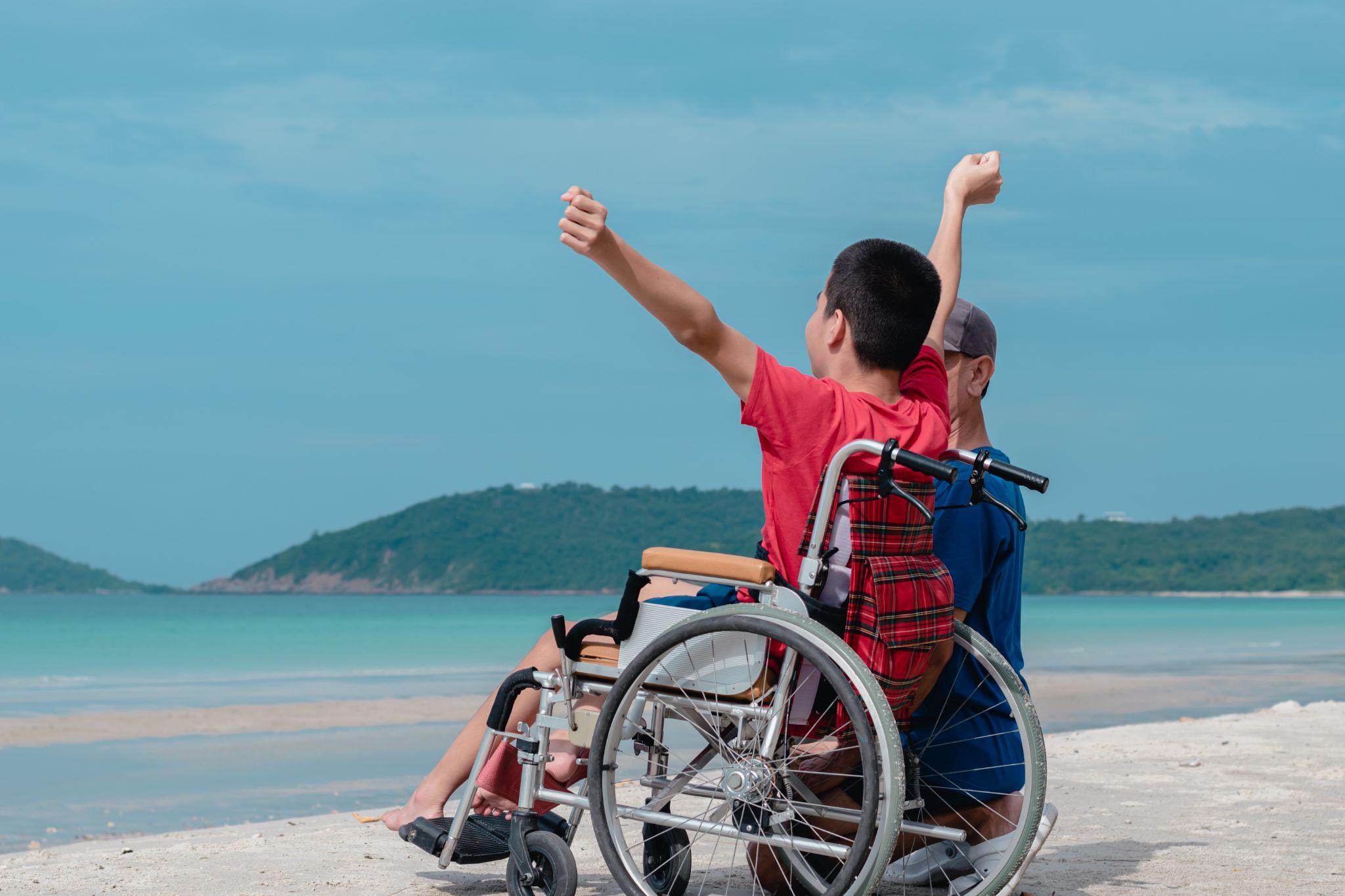 Asian special child on wheelchair is smiling, playing, doing activity on sea beach with father
