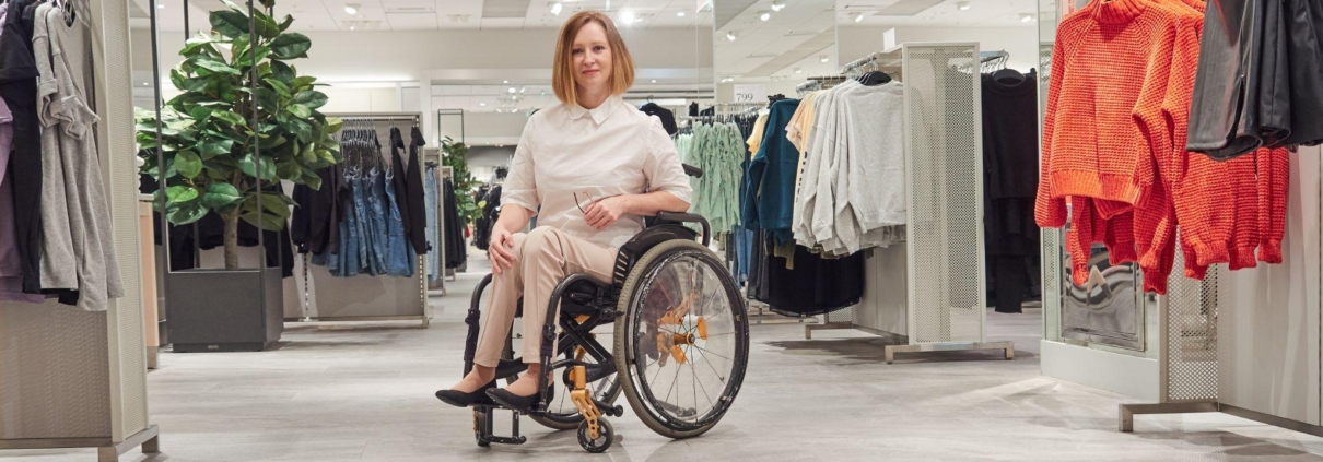 Woman shopper in a wheelchair chooses clothes in the mall